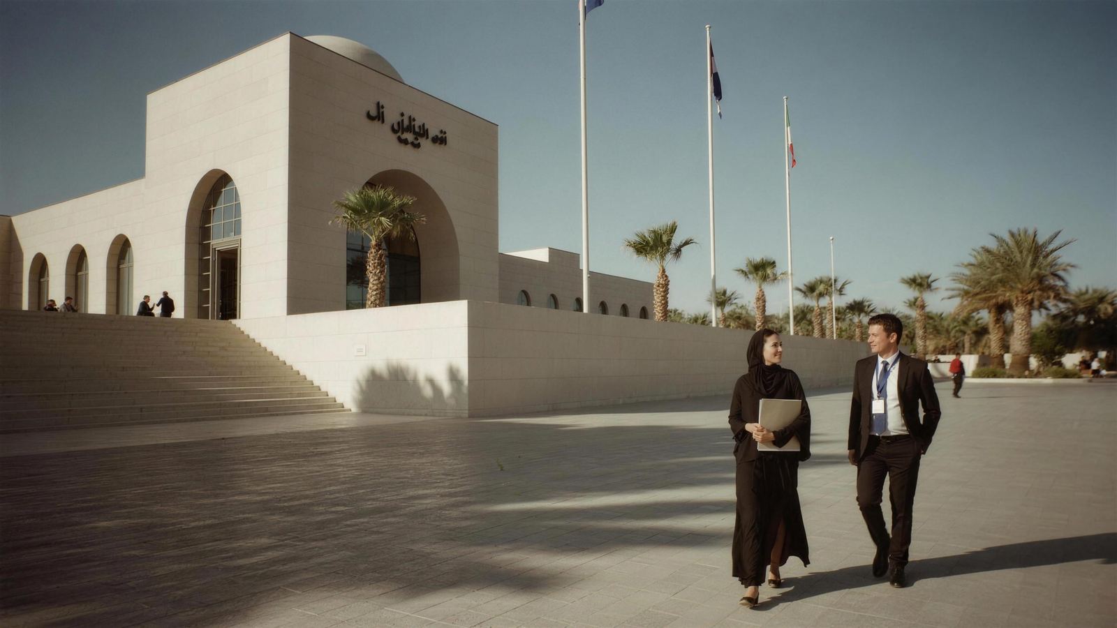 A ministry plaza in pale stone, an Emirati woman in an abaya walking in conversation with a suited colleague